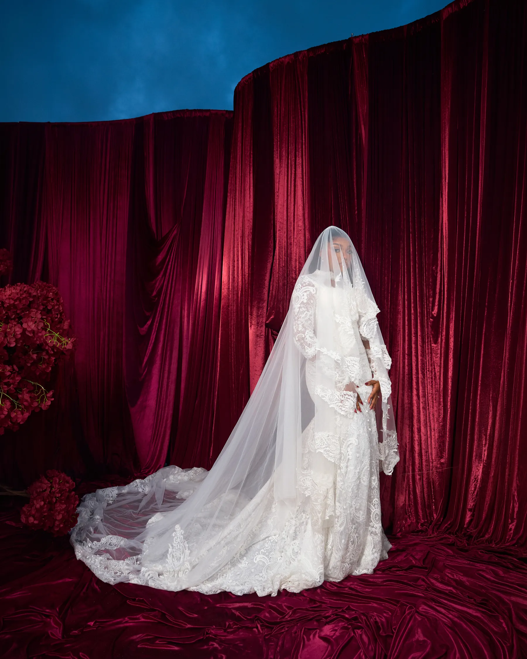 The same Jiofit lace gown from the side, the veil over the bride’s face and the train spread across the velvet floor